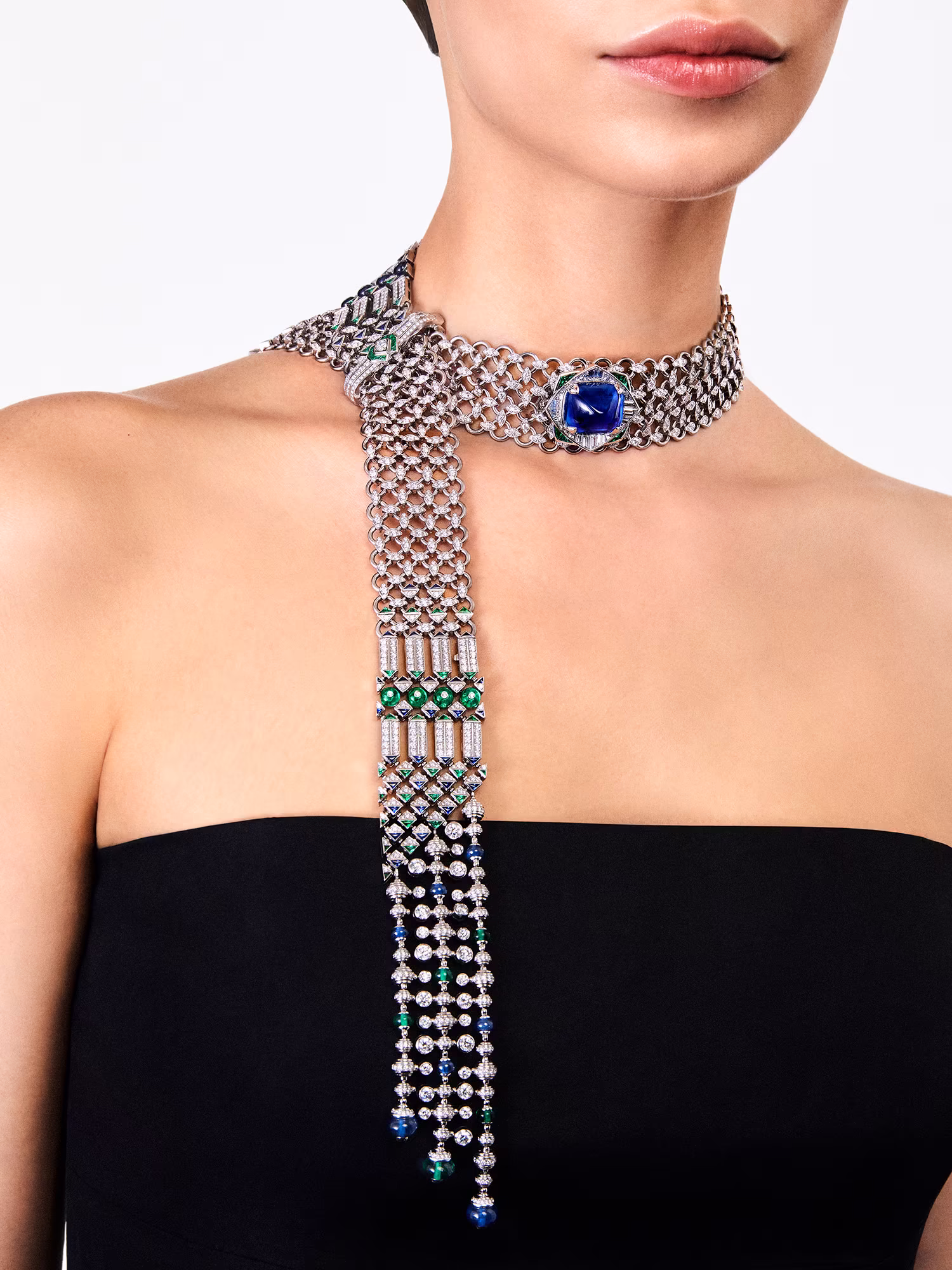 Model wearing a black dress with a diamond choker necklace featuring a large blue sapphire and pendants with blue and green stones.