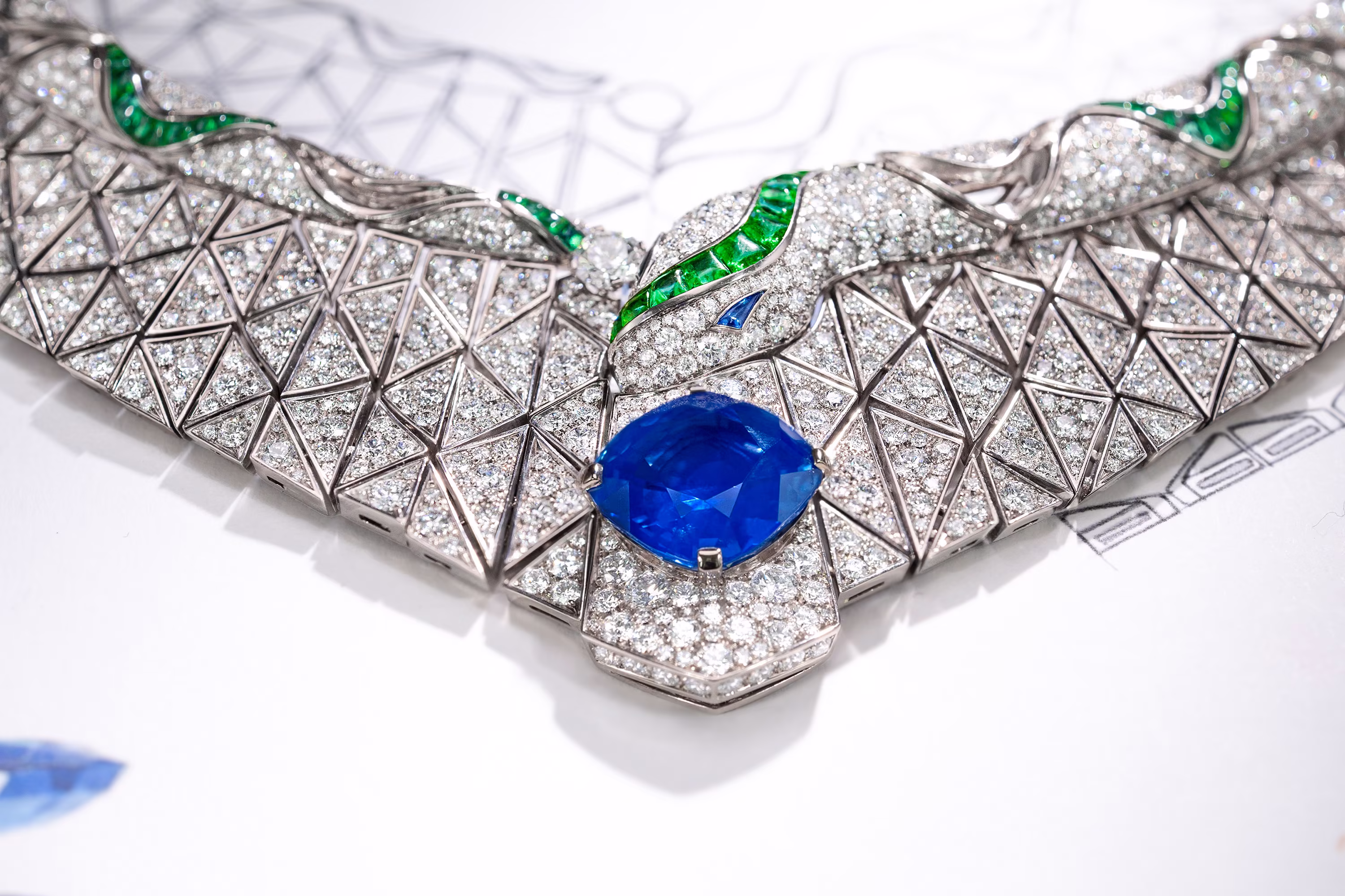 Detail of necklace with diamonds and green inserts; in the center, a large blue stone set above the technical drawing.