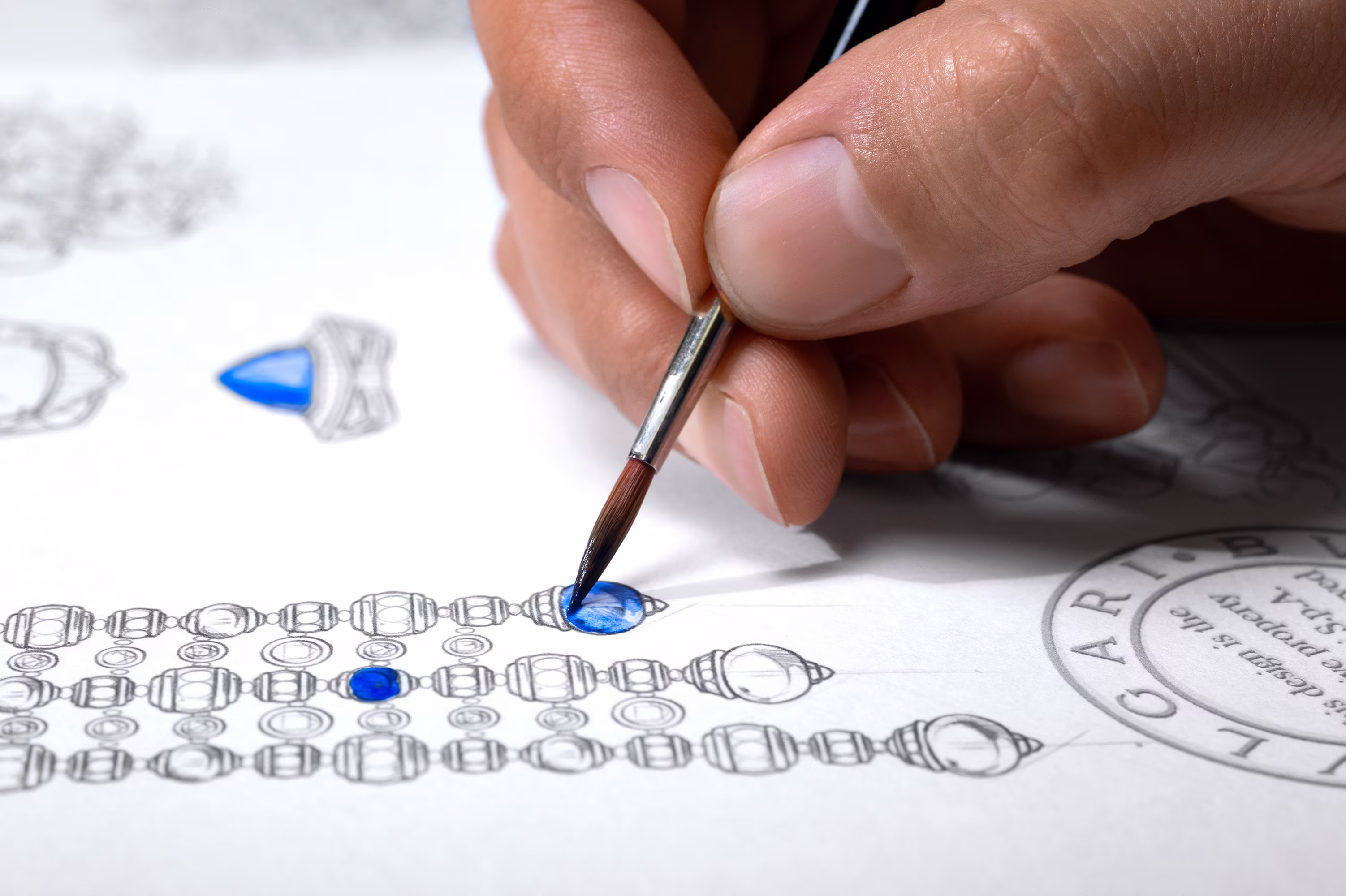 Hand painting a blue gemstone on a detailed jewelry sketch with a fine brush, highlighting the design of a luxury necklace.